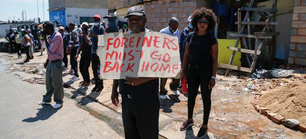 Anti-migrant protester holding a Foreigners must got back home" poster on a South African township steet